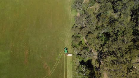 Eine-Luftaufnahme-Aus-Der-Vogelperspektive-Eines-Traktors,-Der-Trockenes-Gras-Neben-Buschland-Im-Ländlichen-Australien-Schneidet