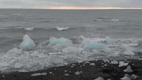 Slow-motion-shot-flying-towards-the-waves-crashing-into-icebergs-on-the-beach