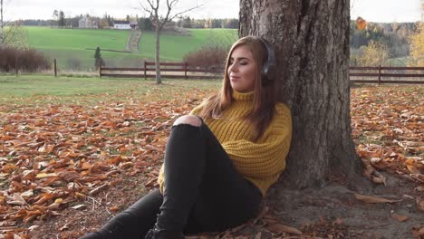 Erwachsenes-Mädchen-Sitzt-Unter-Dem-Baum-Und-Hört-Hörbücher-Oder-Musik-In-Der-Herbstlandschaft-Und-Entspannt-Sich