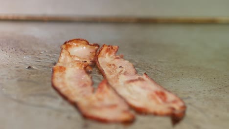 Close-up-of-bacon-sizzling-on-a-restaurant-grill-and-flipped-with-tongs
