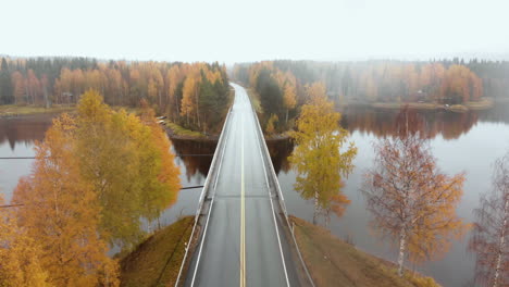 Aerial,-decreasing,-drone-shot,-above-a-bridge,-surrounded-by-mist-and-autumn-colors,,-on-a-foggy,-misty-and-cloudy,-fall-day,-at-lake-Pielinen,-in-Nurmes,-North-Karelia,-Finland