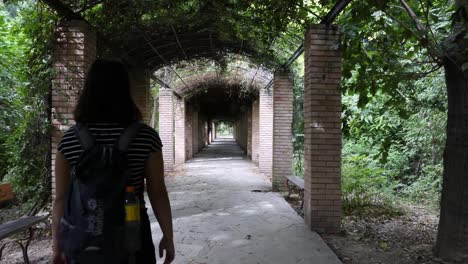 Slowmotion-following-shot-of-an-young-asian-woman-with-a-backpack-who-walks-through-a-tunnel-with-a-lot-of-plants-on-the-side