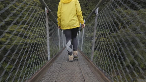 Low-angle-shot-of-girl-in-yellow-jacket-walking-across-bridge-in-New-Zealand