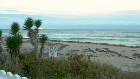Tropical-beach-at-sunset-with-an-End-of-Guarded-Beach-sign-posted