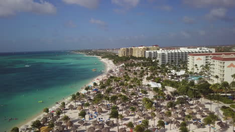 Highrise-hotels-with-palm-trees-blowing-in-the-wind-along-the-beach-in-Aruba