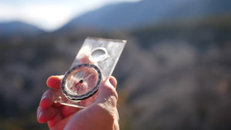 Nahaufnahme-Einer-Hand,-Die-Einen-Zerkratzten-Magnetkompass-Hält,-Mit-Dem-Epischen-Wald-Und-Den-Bergen-Kaliforniens-Im-Hintergrund