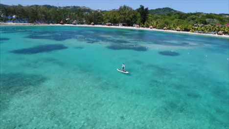 Luftaufnahme-In-Zeitlupe-Von-Menschen,-Die-In-Der-Nähe-Des-Strandes-Eines-Resorts-Am-Honduranischen-Karibischen-Meer-Paddeln