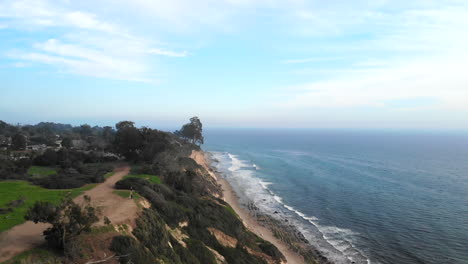 Aerial-drone-shot-over-the-beach-cliffs-of-the-Douglas-Preserve-in-Santa-Barbara,-Californai-with-blue-ocean-waves-crashing-below
