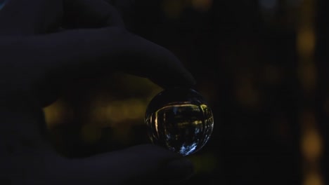 close-up-of-a-young-female-hand-holding-a-small-crystal-ball-reflecting-landscape-in-an-autumnal-forest-while-spinning-around