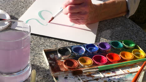 Una-Anciana-Artista-Pintando-Con-Acuarelas-Vibrantes-Para-Relajarse-Y-Liberar-El-Estrés-En-Un-Estudio-De-Arte-Al-Aire-Libre