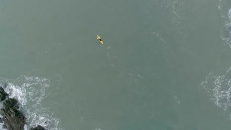 Top-down-of-a-person-rowing-a-yellow-kayak-between-two-rocky-areas-that-are-creating-choppy-waters