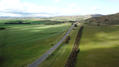 Drone-Pan-Around-Highway-With-Cars-Driving-Down-Road-Surrounded-By-Green-Fields-And-Trees