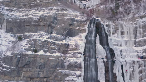 Eiskletterer-Hängen-Gefährlich-An-Einem-Gefrorenen-Wasserfall-In-Den-Felsigen-Bergen-Und-Rutschen-Nach-Oben