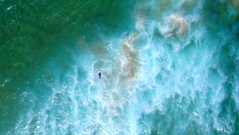 AERIAL:-Birdseye-view-from-80-metres-of-surfer-battling-the-waves,-current-and-white-wash-in-a-turbulent-ocean