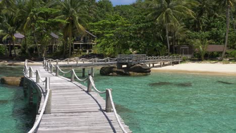 Wooden-bridge-leading-onto-a-tropical-white-sand-beach-island
