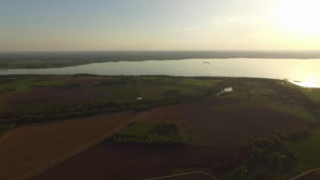 Paraglider-approaching-lake-wide-shot-aerial-view