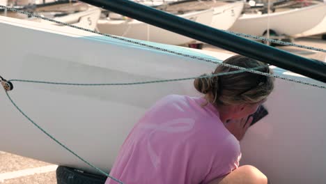 A-young-woman-sailor-scrubbing-and-cleaning-the-hull-of-her-sailboat-in-slow-motion-after-sailing-in-a-regatta