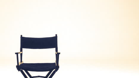 A-single-director's-folding-chair-in-front-of-a-plan-white-backdrop-with-some-warm-lighting