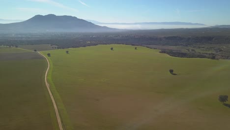 Aerial-view-of-an-extense-meadow-in-a-sunny-hazy-day-with-mountains-in-the-background