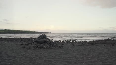 Stacked-rocks-on-a-black-secluded-black-sand-beach-at-sunset