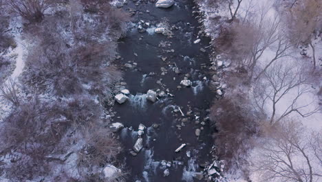Looking-straight-down-at-a-river-rushing-along-a-valley-in-winter---zooming-out