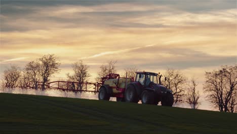 A-farmer-with-a-tractor-spraying-chemicals-to-a-field-during-sunset