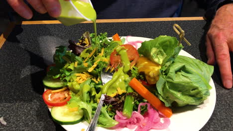 Eine-Männliche-Hand-Gießt-Grünes-Dressing-über-Frischen-Salat-Mit-Salat,-Zwiebeln-Und-Tomaten-Für-Eine-Gesunde-Vorspeise