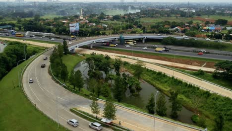 Unveiling-aerial-drone-shot-of-curvy-highway,-bridge,-and-small-lake-with-green-trees-at-Alam-Sutera-in-the-day