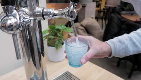 man-pouring-fizzy-water-from-a-modern-tap-in-a-blue-glass