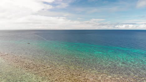 drone-horizon-shot-of-shallow-blue-tropical-ocean-under-blue-sky-and-white-clouds-as-Philippine-pump-boat-floats-near-the-coral-in-the-Pacific