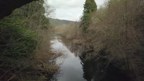 Aerial-footage-flying-beneath-a-disused-bridge-on-the-River-Foyers-looking-towards-Loch-Ness,-Scottish-Highlands,-Scotland