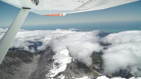 SLOWMO---Aerial-shot-from-plane-scenic-flight-over-west-coast-Franz-Josef,-Aoraki-Mount-Cook,-National-Park-with-clouds,-snowcapped-rocky-mountains-and-ocean-in-background