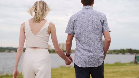 Beautiful-young-couple-walking-and-holding-hands-near-a-lake