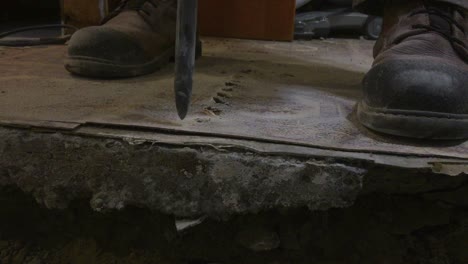 Medium-close-up-on-drill-bit-penetrating-basement-concrete-floor-creating-dust-and-smoke,-with-hand-entering-frame-lifting-up-tile