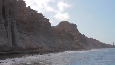 Una-Playa-De-Arena-Negra-En-Santorini,-Grecia,-Rodeada-De-Formaciones-De-Acantilados-Volcánicos-Blancos