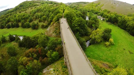 Descending-Aerial-view-cyclists-and-hikers-crossing-Headstone-Viaduct,-bridge-in-the-Derbyshire-Peak-District-National-Park,-Bakewell