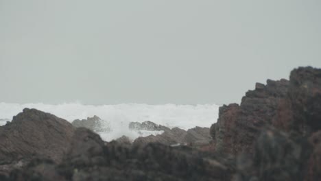 Waves-crashing-on-beach-with-rocks-in-foreground