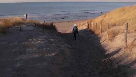 Young-woman-walking-down-to-beach-with-trash-bags-on-sunny-winter-day
