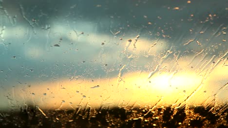 Rain-water-hitting-a-windshield-while-a-car-is-driving-at-sunset
