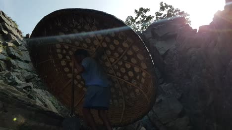 A-man-carrying-a-coracle-on-one-hand-and-paddle-on-the-other-hand-while-climbing-steps-in-in-Hogenakkal,-Tamilnadu,-India