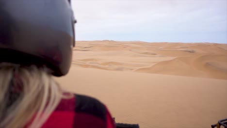 Slomo-over-the-Shoulder-of-Young-Blond-Woman-with-Helmet-on-Quad-Bike-overlooking-Namibian-Desert