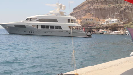 A-luxury-yacht-is-backing-up-to-park-in-a-small-Greek-sea-port,-on-the-island-of-Santorini