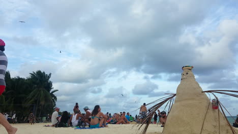 Crowded-Beach-In-Mexico-On-A-Sunny-Day-With-A-Snowman-Made-Of-Sand