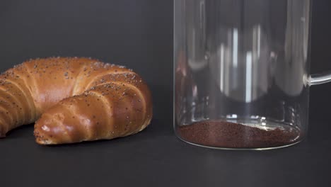 CLOSEUP---Filling-french-press-with-ground-coffee-next-to-a-breakfast-roll