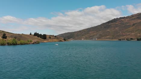 SLOWMO---Aerial---Boat-on-Lake-Dunstan,-Central-Otago,-New-Zealand-with-mountains-and-clouds-in-background