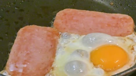 Spam-In-Zeitlupe-Und-In-Einer-Bratpfanne-Brutzelnde-Eier-Eier-Mit-Der-Sonnenseite-Nach-Oben-Frühstück-Mit-Hohem-Cholesterinspiegel
