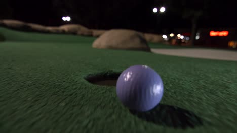A-purple-mini-golf-ball-falls-into-the-golf-hole-and-bounces-in-the-pocket-on-a-course