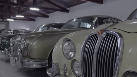 Low-angle-panning-shot-across-lined-up-collection-of-stylish,-classic-Jaguar-vehicles-parked-in-personal-showroom