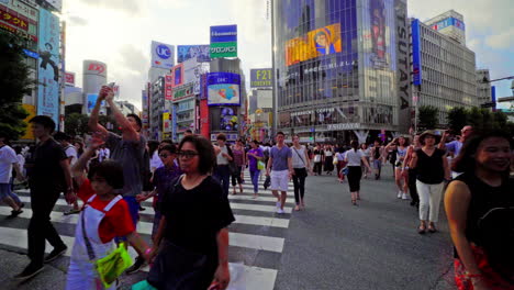 Schrägaufnahme-Mit-Hohen-Shibuya-Gebäuden-Und-Menschen,-Die-Eine-Stark-Befahrene-Straße-überqueren