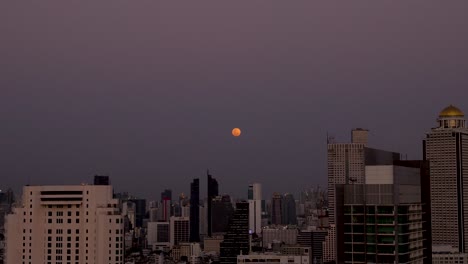 Evening-to-night-timelapse-of-red-twilight-moon-rising-behind-Pullman-Bangkok-Hotel-G,-Bang-Rak,-Bangkok